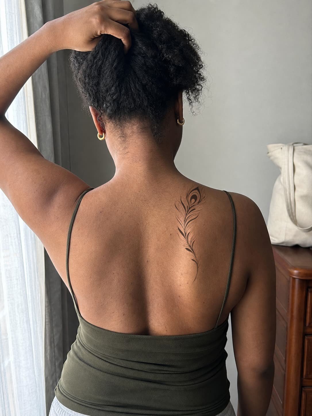 Healed black feather tattoo preview aligned with the upper back and shoulder blade